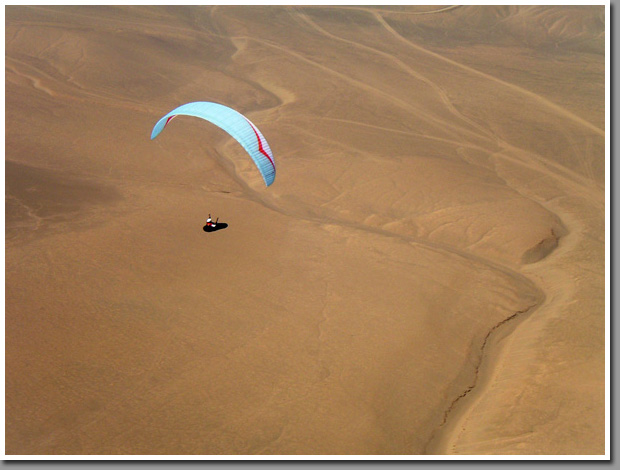 Pilot Mike Christiansen flying his paraglider over desert plateau near Patillos launch 60km south of Iquique during Copa Altazor 2008 competition, Atacama Desert, Iquique, Chile
