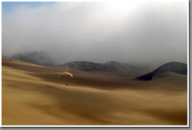 Paraglider soaring inland mountain dunes covered by incoming camanchaca mist, Atacama Desert, Chile