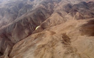 Winter is over - Carlos Curi flying his paraglider over a desert plateau near Iquique, The Atacama Desert, Chile